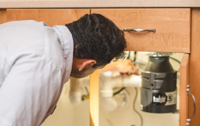 A technician looking at the plumbing under a kitchen sink