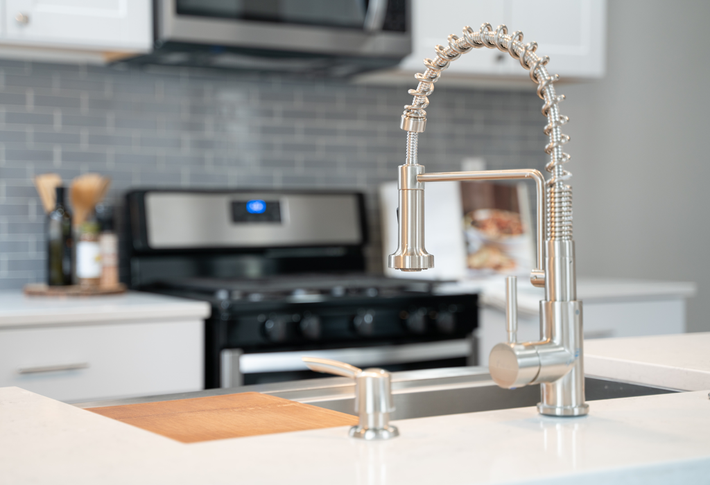 Picture of a kitchen sink on a white island, with a black oven and white countertops in the background.
