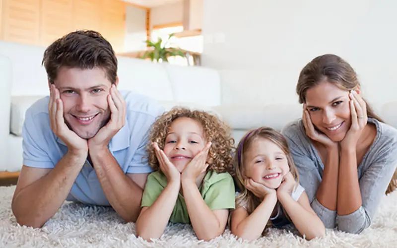 family laying on a rug smiling at the camera