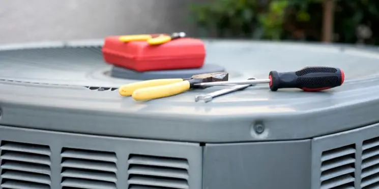 Outdoor HVAC unit with some tools laying on top of it, including pliers, a wrench, and a screwdriver.
