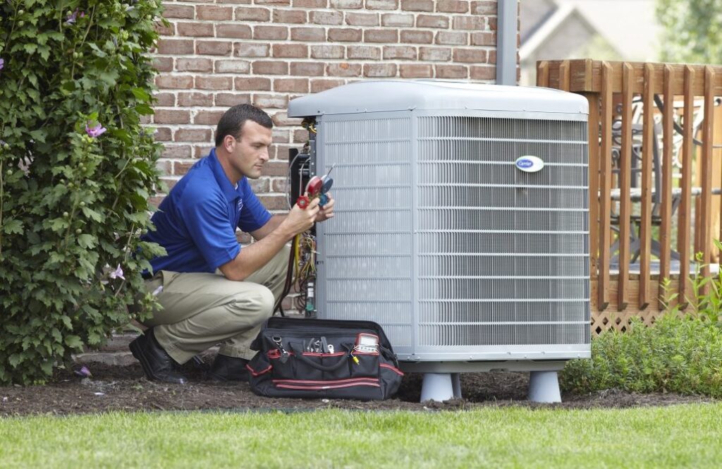 An HVAC technician is kneeling next to an outdoor HVAC unit, performing maintenance.