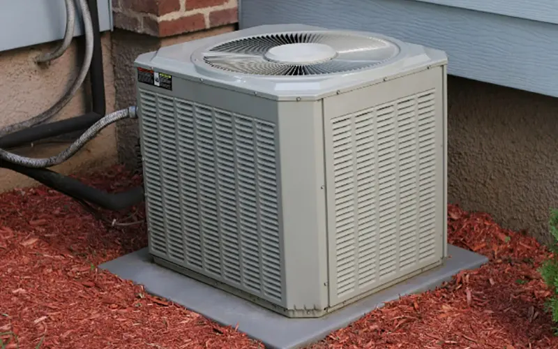 Outdoor AC unit on a concrete slab, surrounded by red mulch, next to a home.