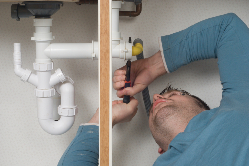 Plumber at work under a sink