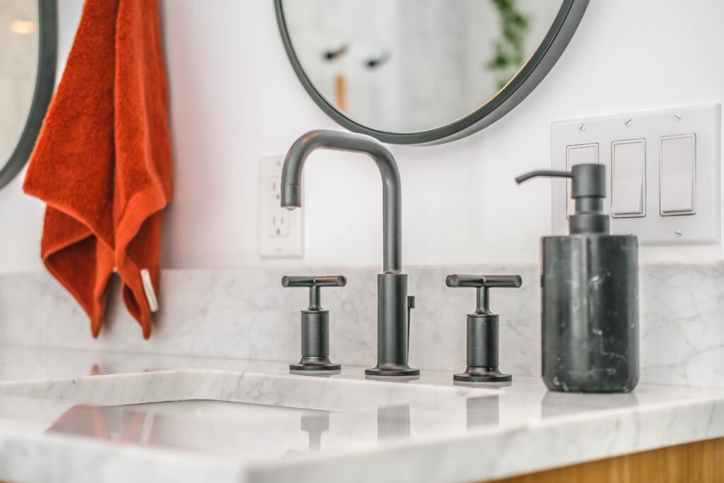 Black bathroom faucet with two black faucet handles on a white porcelain sink. 