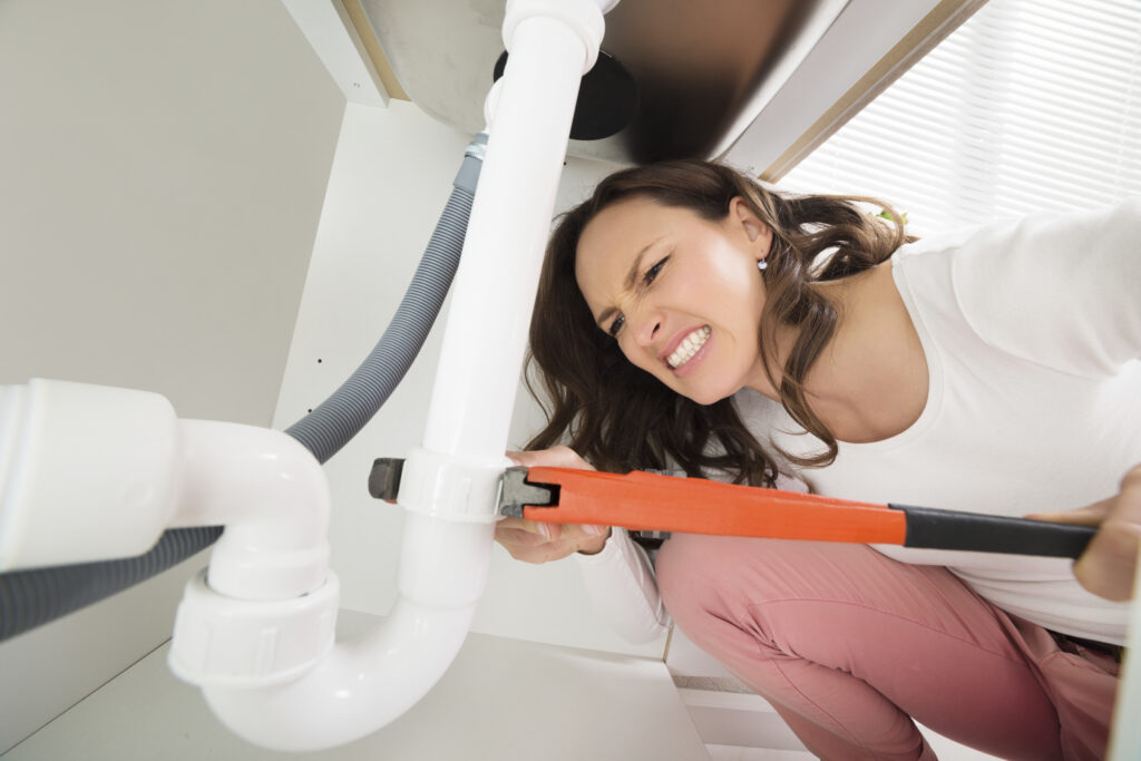 Close-up of a homeowner with a monkey wrench tightening a white pipe under the sink
