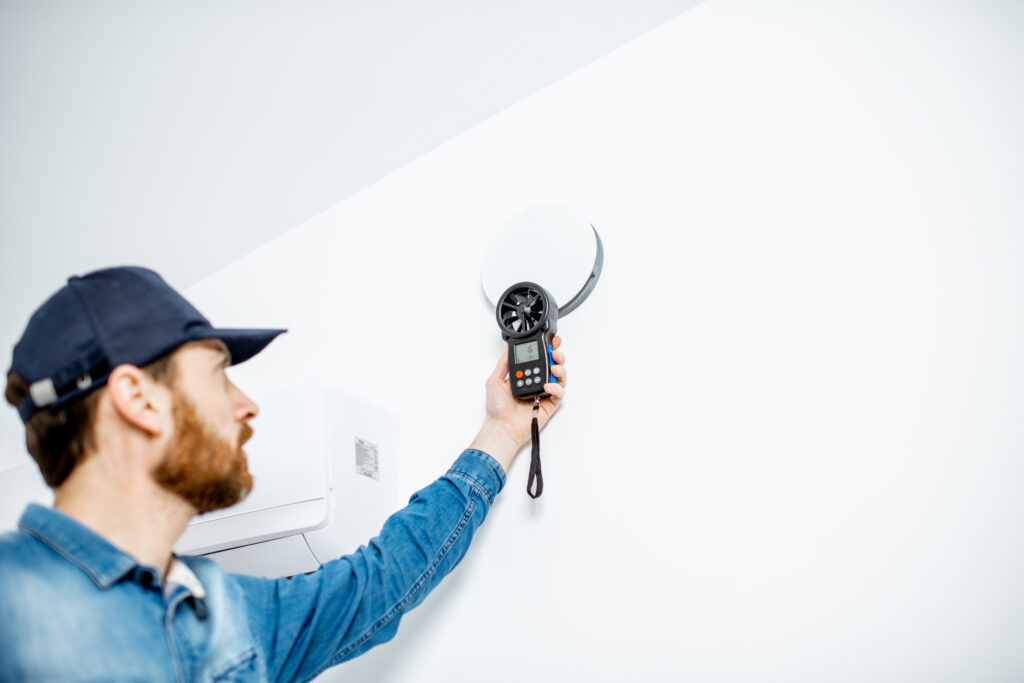 Technician checking the speed of air ventilation with measuring tool on the white wall background