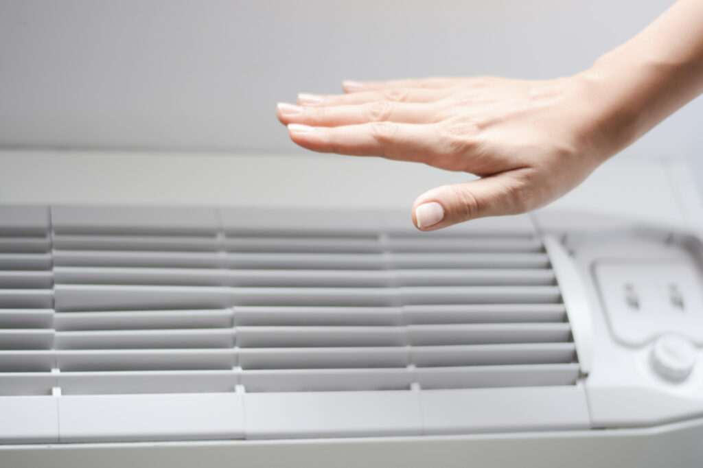 Person checking to see if cold air is coming from their air conditioner by putting their hand over the vents. 