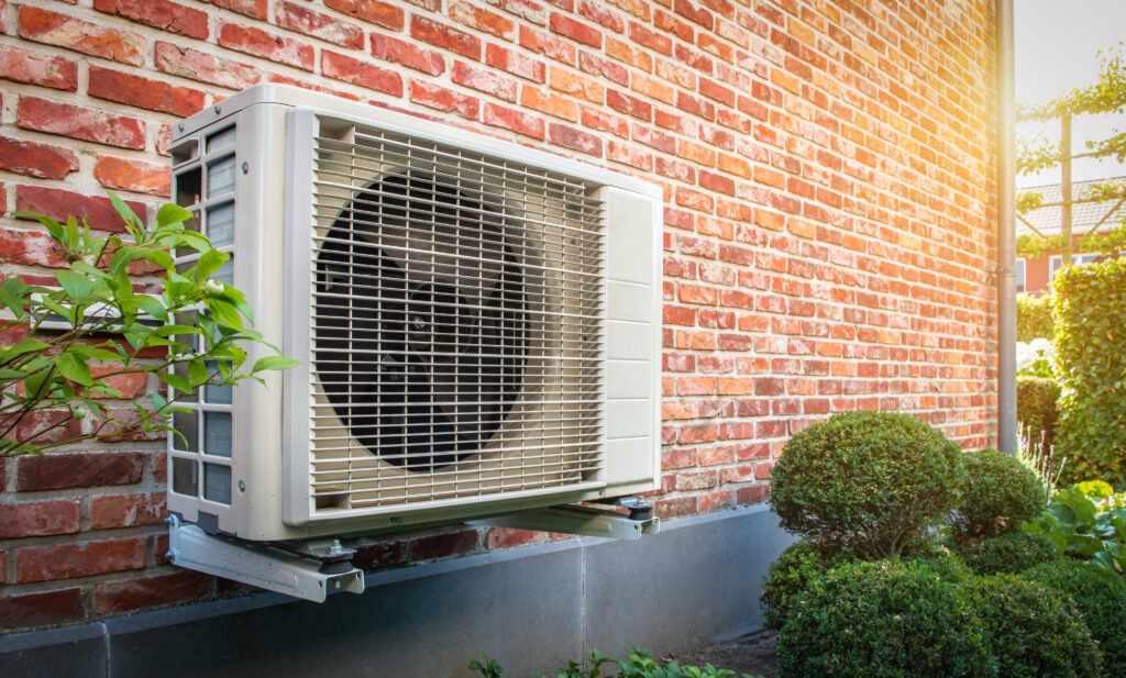 Side view of outdoor heat pump unit hanging on brick wall of house on a sunny day. 