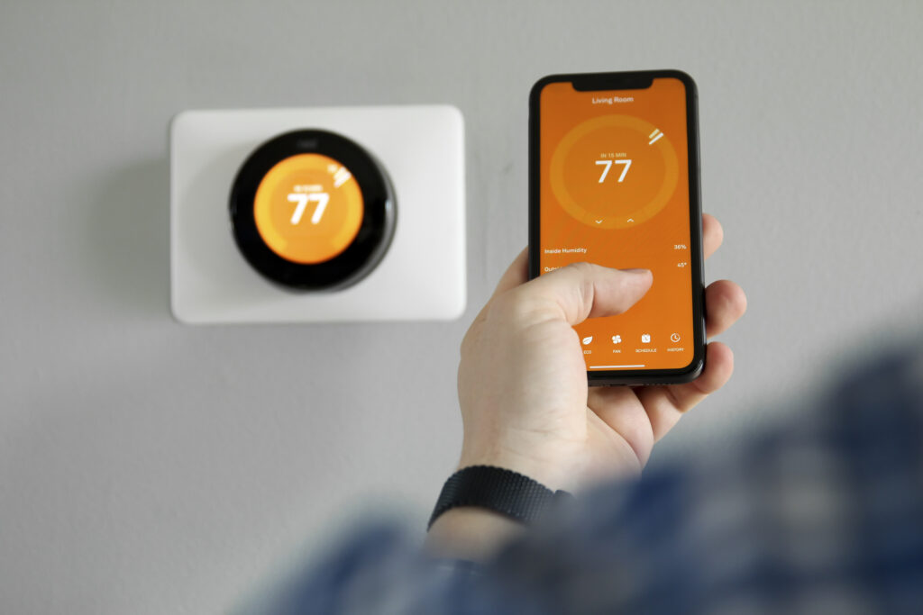 Person uses a mobile phone with smart home app to control their thermostat