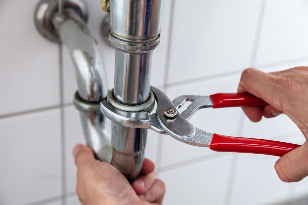 Close-up of a plumber’s hand repairing sink with adjustable wrench