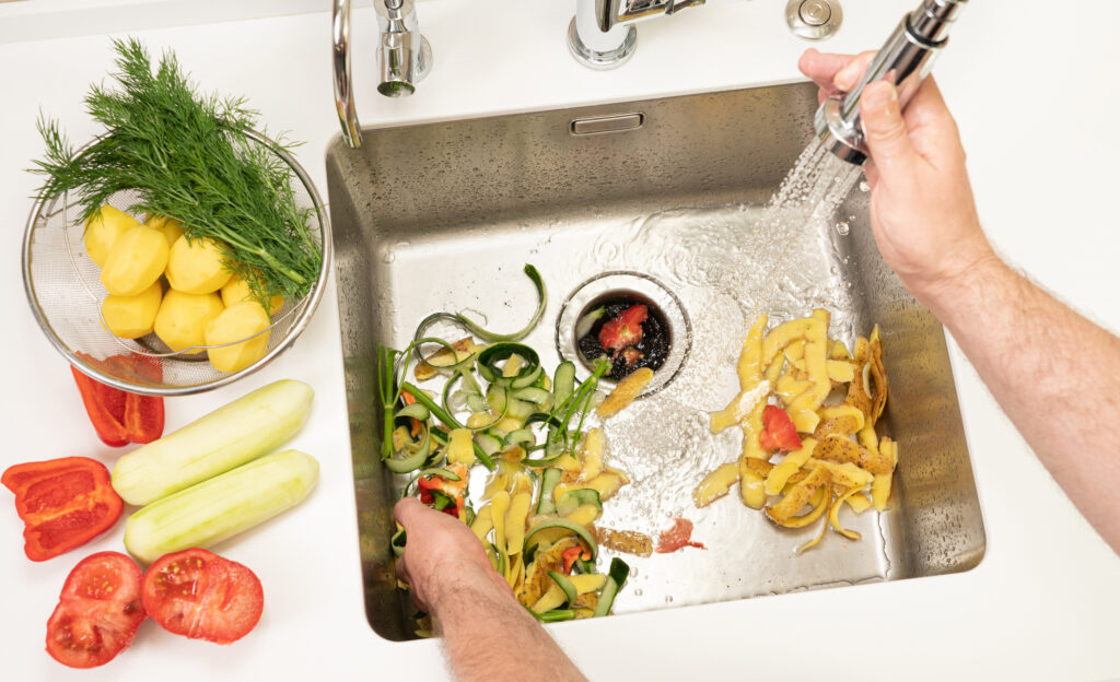 A person recycles food waste using a modern garbage disposal, rinsing vegetable peels down the drain