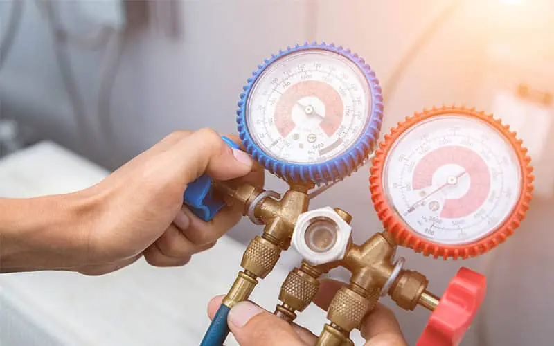 A pair of hands holding an AC unit gauge with red and blue sides.